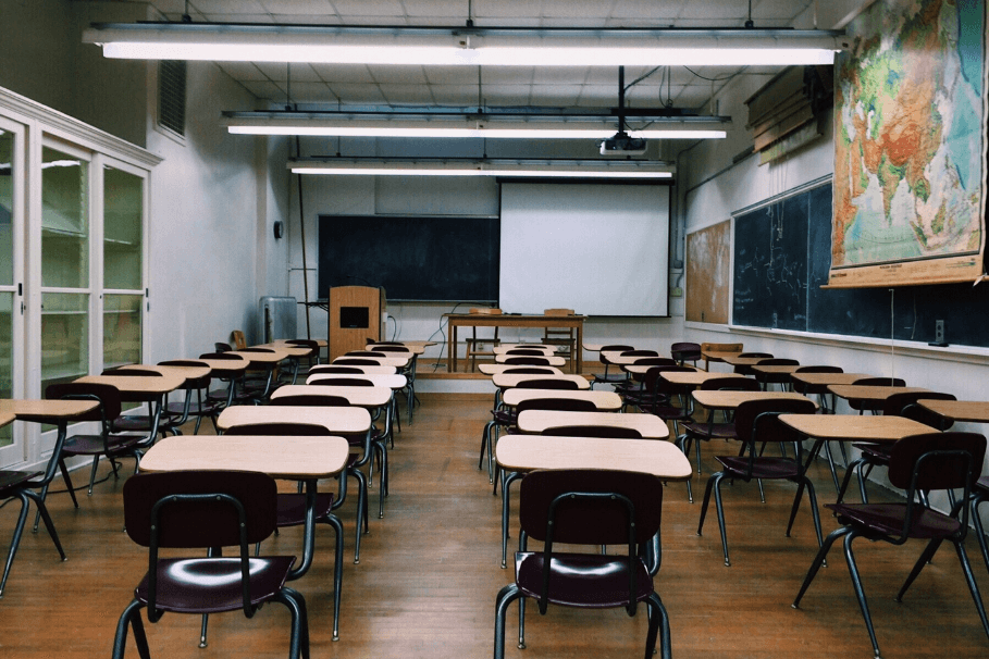 Clean and organised classroom with desks, chairs, and a projector screen in a school setting.