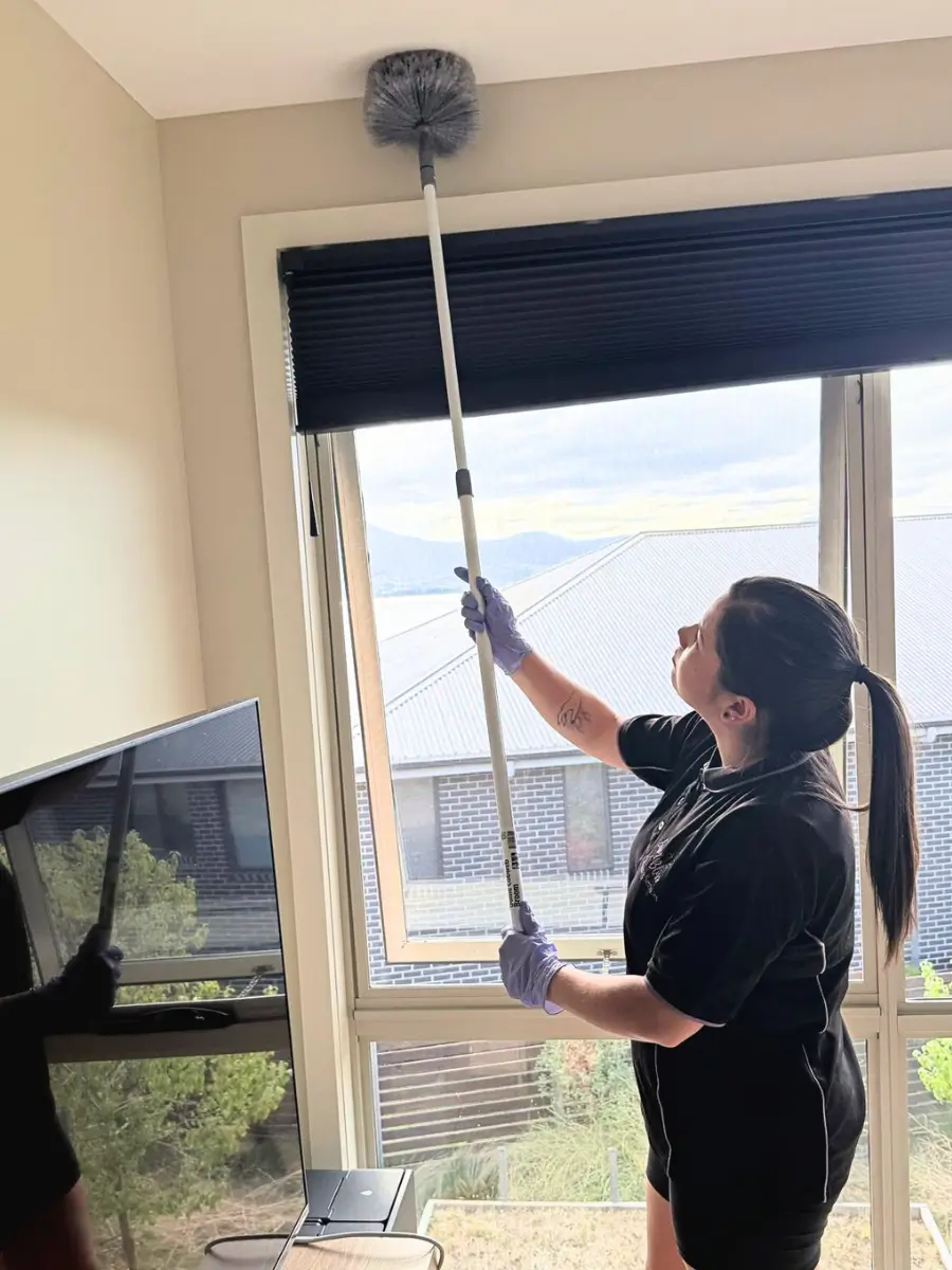 Cleaner dusting a ceiling with an extendable duster